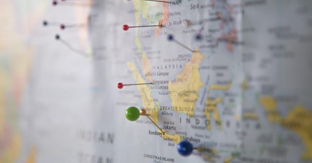 A paper map of the world is hanging on the wall, and the image is focused in on Malaysia and Indonesia, with other areas out of focus. Pins have been stuck into the map to highlight arbitrary locations.